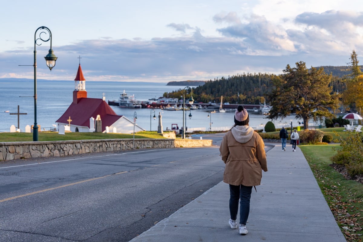 Une personne qui se promène dans le centre-ville, en arrière plan La Chapelle de Tadoussac